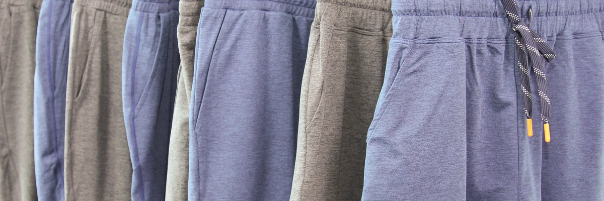 A close-up row of heathered drawstring sweatpants in muted blue, gray, and taupe tones hanging side by side.