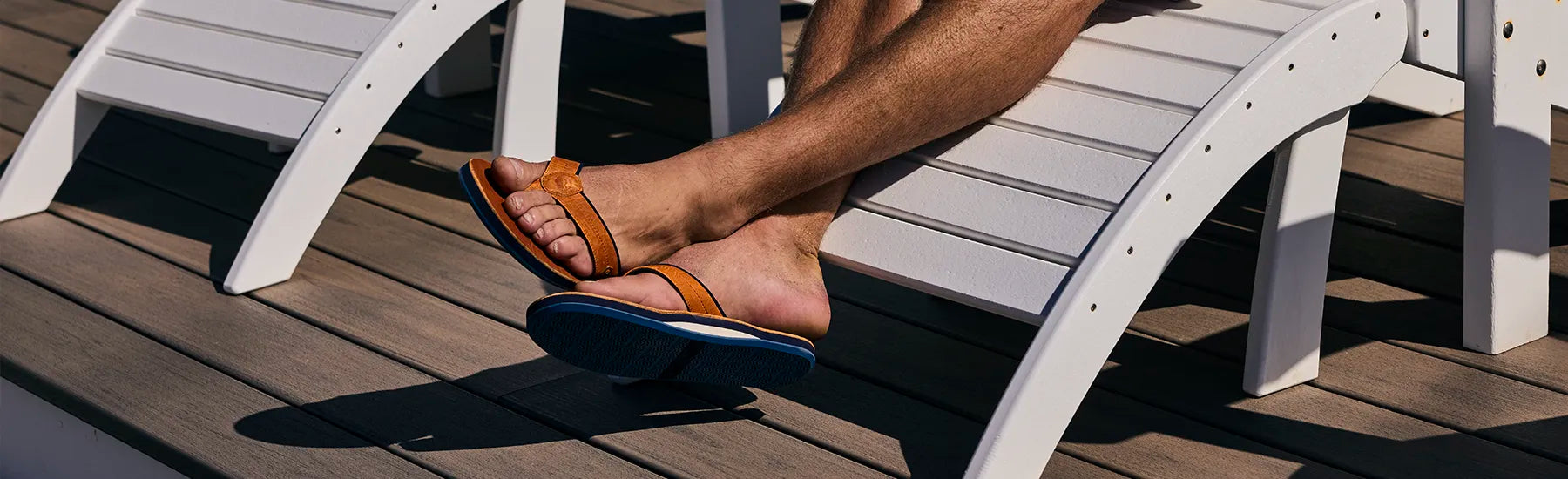 This close-up shot focuses on a person’s legs and feet resting on a white lounge chair, set against a modern wooden deck. The image evokes a feeling of high-end relaxation and leisure.