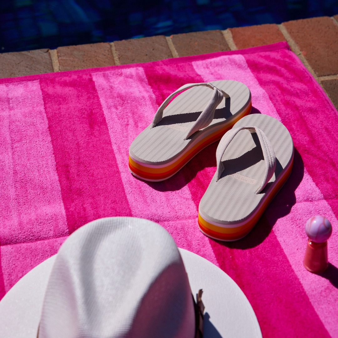 Hari Mari Dunes Sunset flip flops for women sitting on a pink towel next to a pool