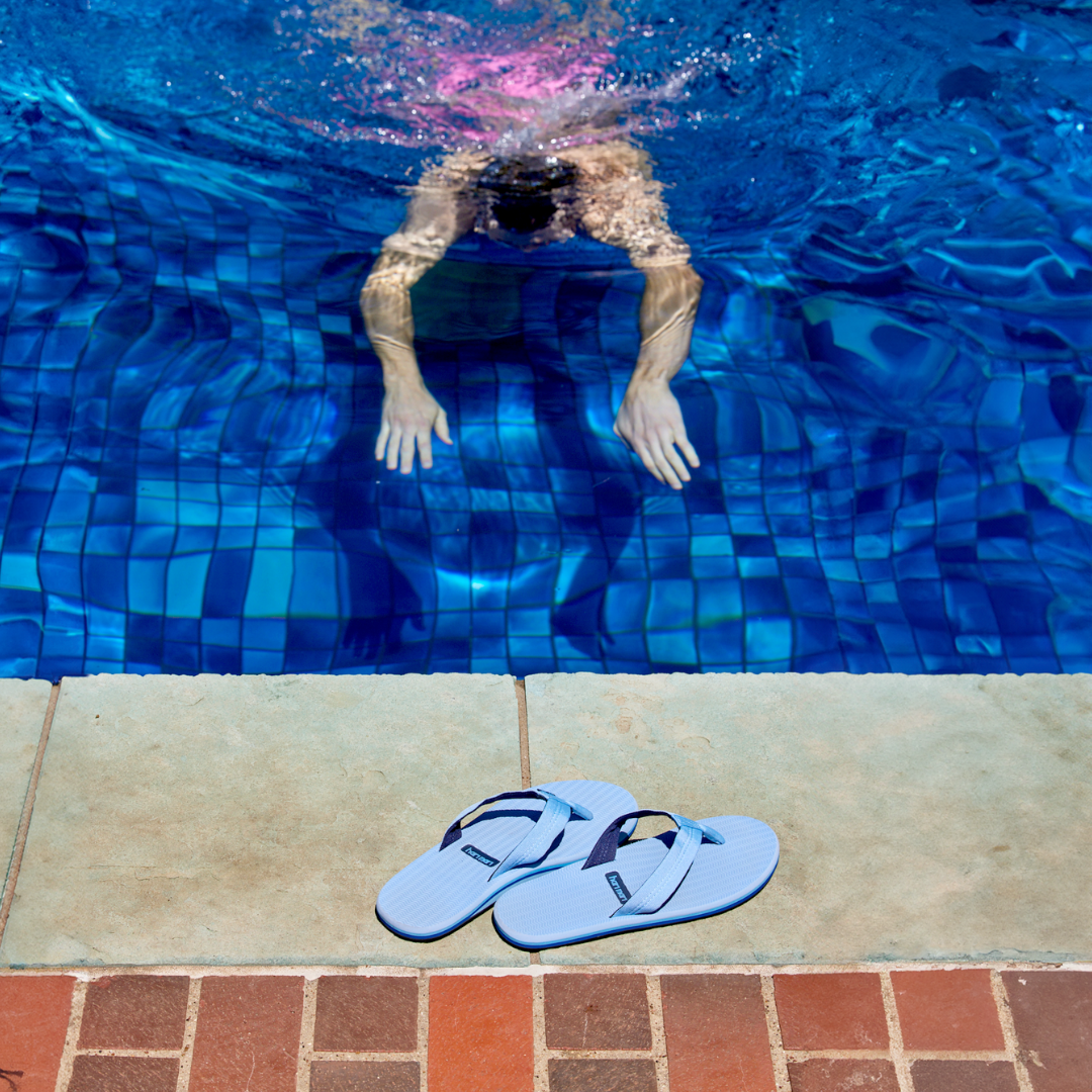 man swimming in a pool with Hari Mari men's waterproof flip flops on the side