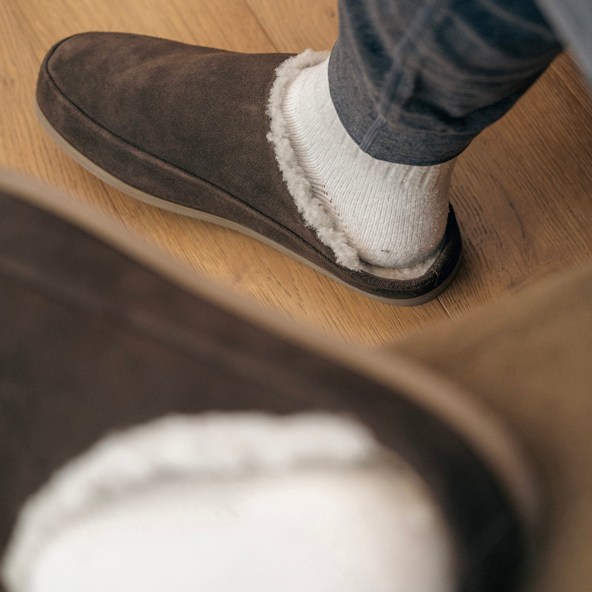 Dark brown Tio Havana slipper with cream plush lining, worn with white socks on a wooden floor.