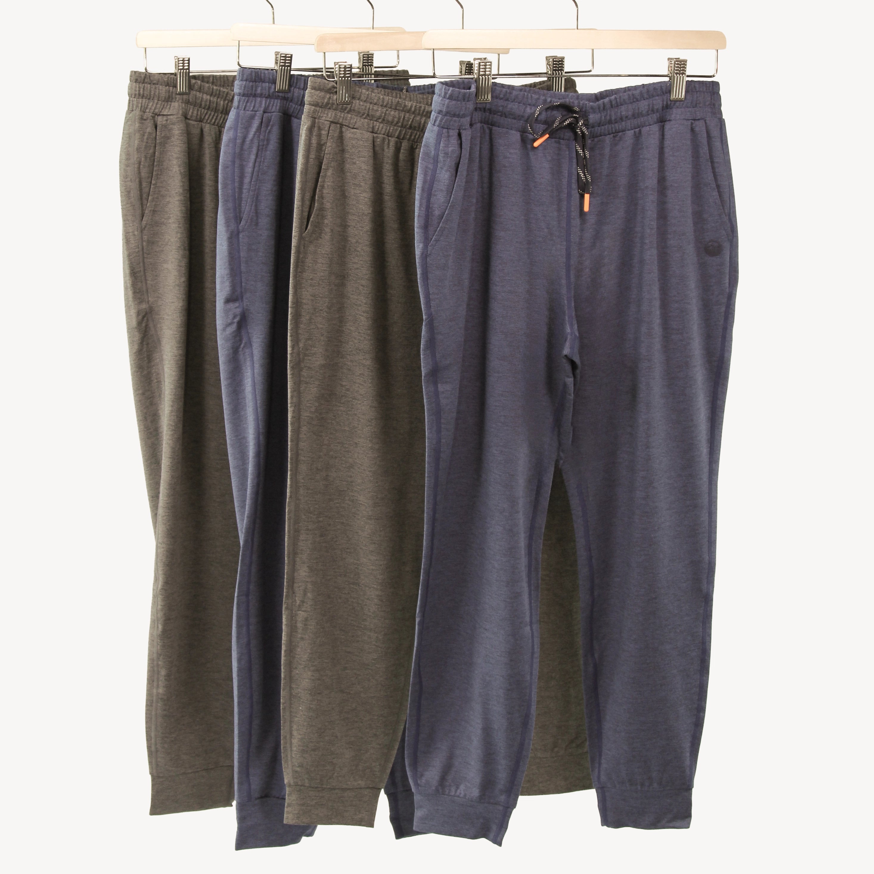 Four pairs of joggers hanging on a wooden hanger against a plain light background. The pants are shown in two different colors: heathered gray and heathered navy blue.