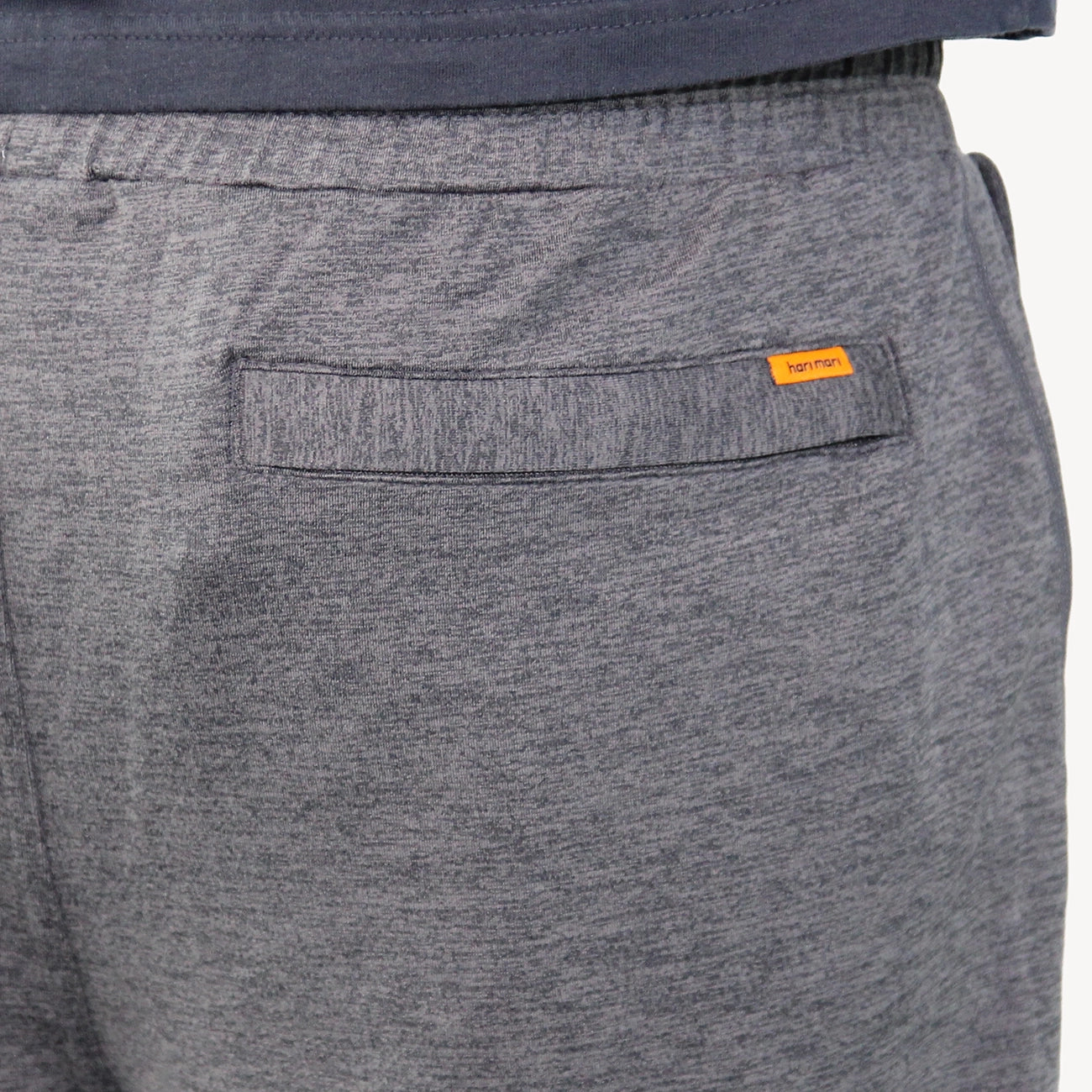 Close-up of heather gray joggers for men showing the back pocket with a small orange Hari Mari brand tab, worn with a navy top.