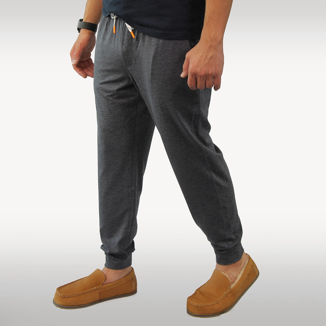 A person wearing dark gray heather joggers with a drawstring waist and elastic cuffs, paired with tan Hari Mari slippers, shown from the waist down against a light gray studio background.