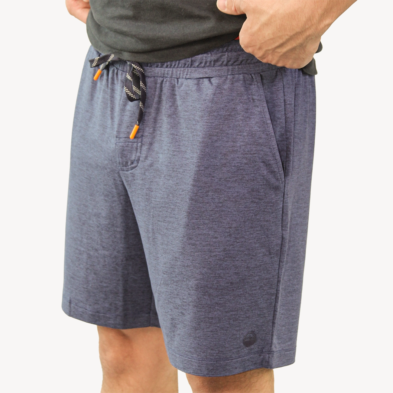 A person wearing dark heather gray drawstring shorts with side pockets, paired with tan Hari Mari flip-flops and a black top, shown from the waist down against a light gray studio background.