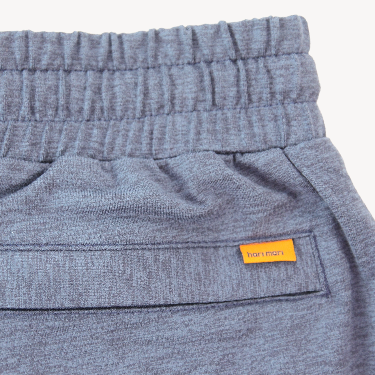 Close-up of heather gray sweatpants showing the elastic waistband, side pocket seam, and a small orange brand tag reading Hari Mari.