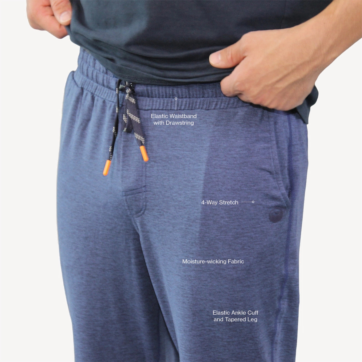 Close-up of a person wearing heathered blue sweatpants with white text callouts highlighting features like the waistband, elastic waistband with drawstring, 4-way stretch, moisture-wicking fabric, and elastic ankle cuff and tapered leg.