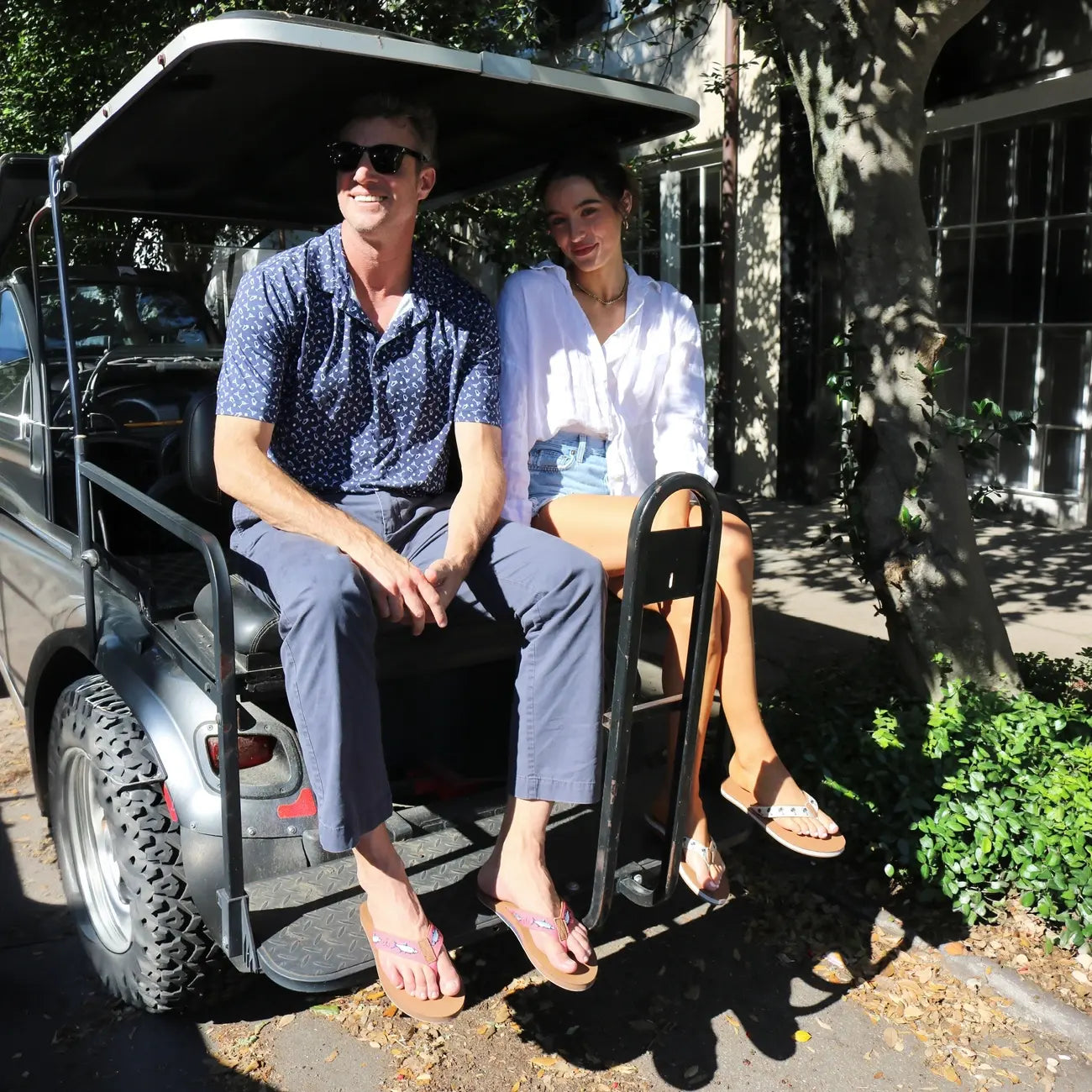 a man and woman wearing Shep Rose x Hari Mari flip flops in a golf cart in charleston