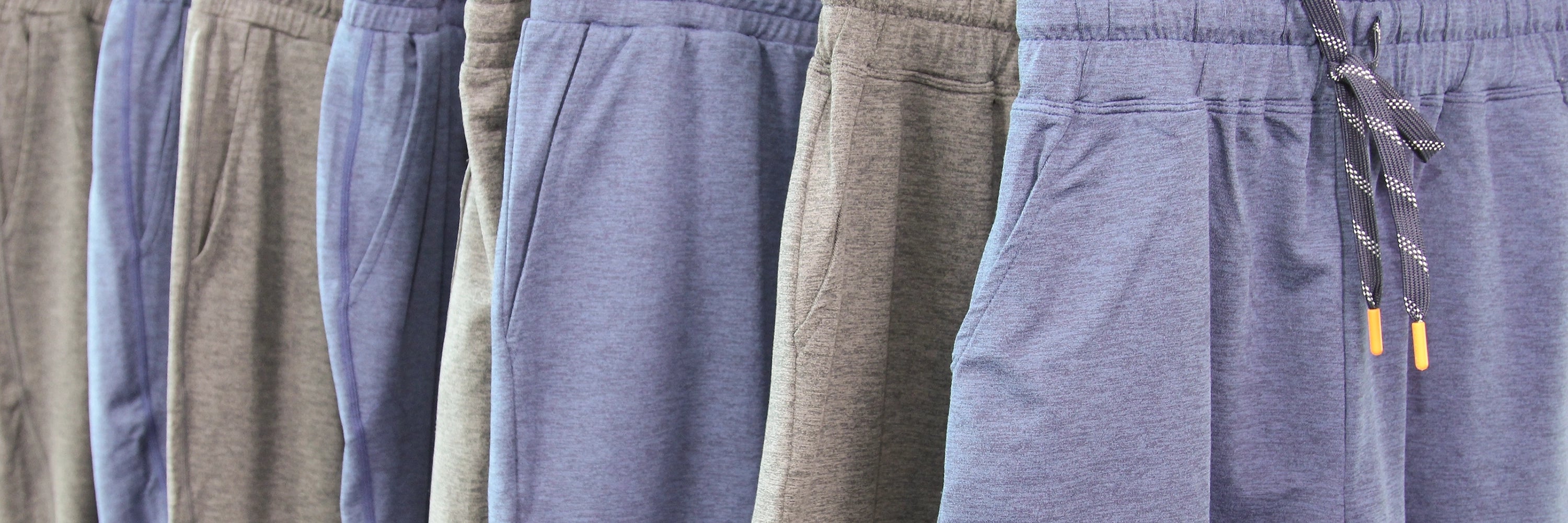 A close-up row of heathered drawstring sweatpants in muted blue, gray, and taupe tones hanging side by side.