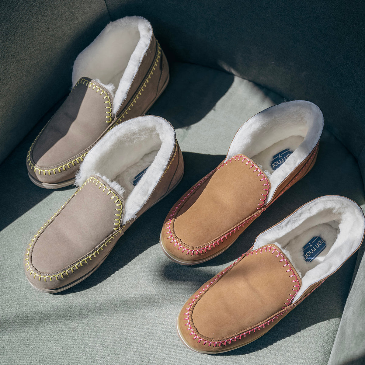 Taupe and tan Tula slippers with cream plush lining and colorful contrast stitching arranged on a chair.