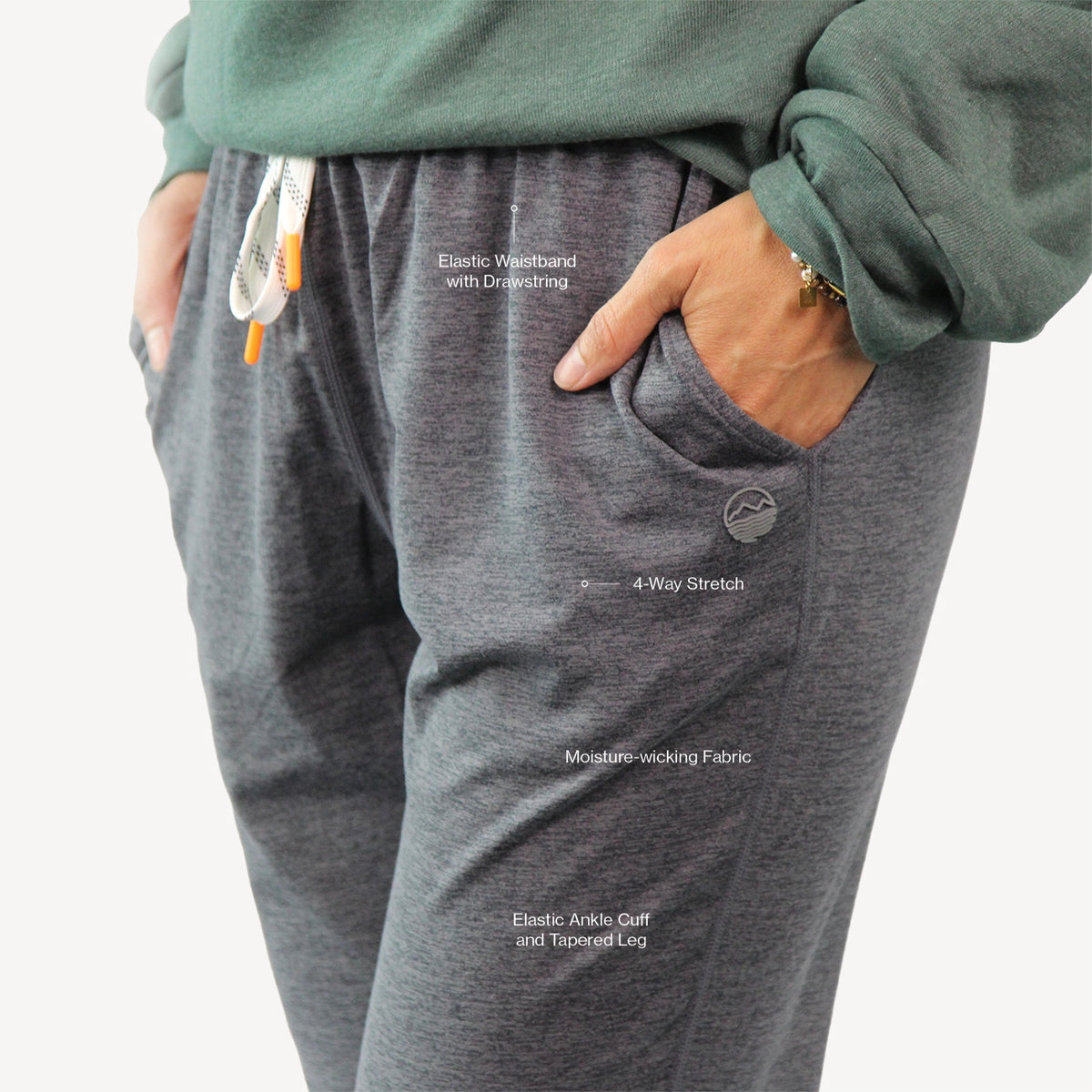 Close-up of a person wearing heather gray jogger sweatpants with side pockets, a white drawstring, and a green sweatshirt partially visible.
