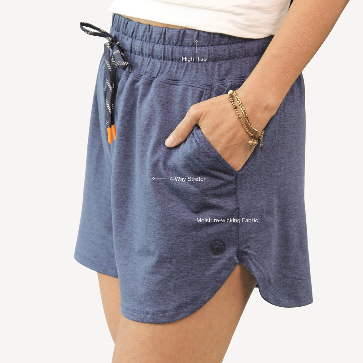 A close-up of a person wearing heathered slate blue athletic shorts with a side pocket, elastic waistband, and drawstring, paired with a white top against a light gray background.