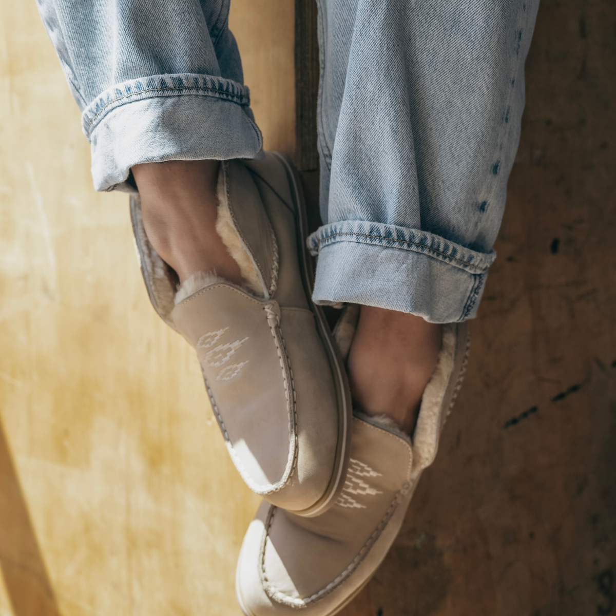 Person wearing tan men's slippers with cuffed jeans outdoors.