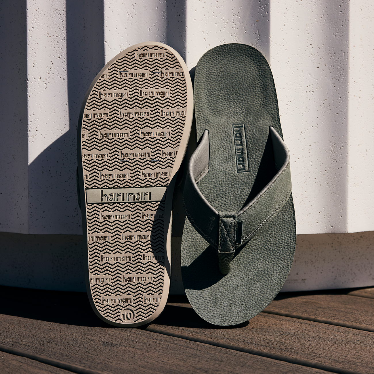 Green leather flip flops from Hari Mari with patterned sole on a wooden surface and striped background