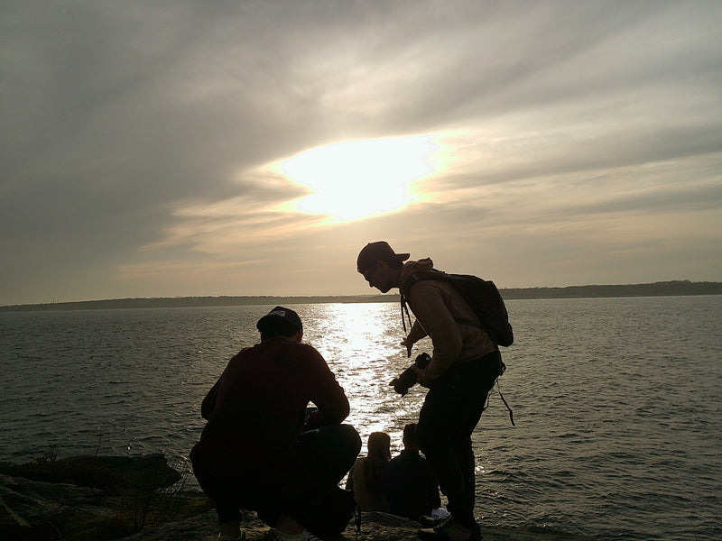Two silhouettes of people by the ocean with a sunset in the background