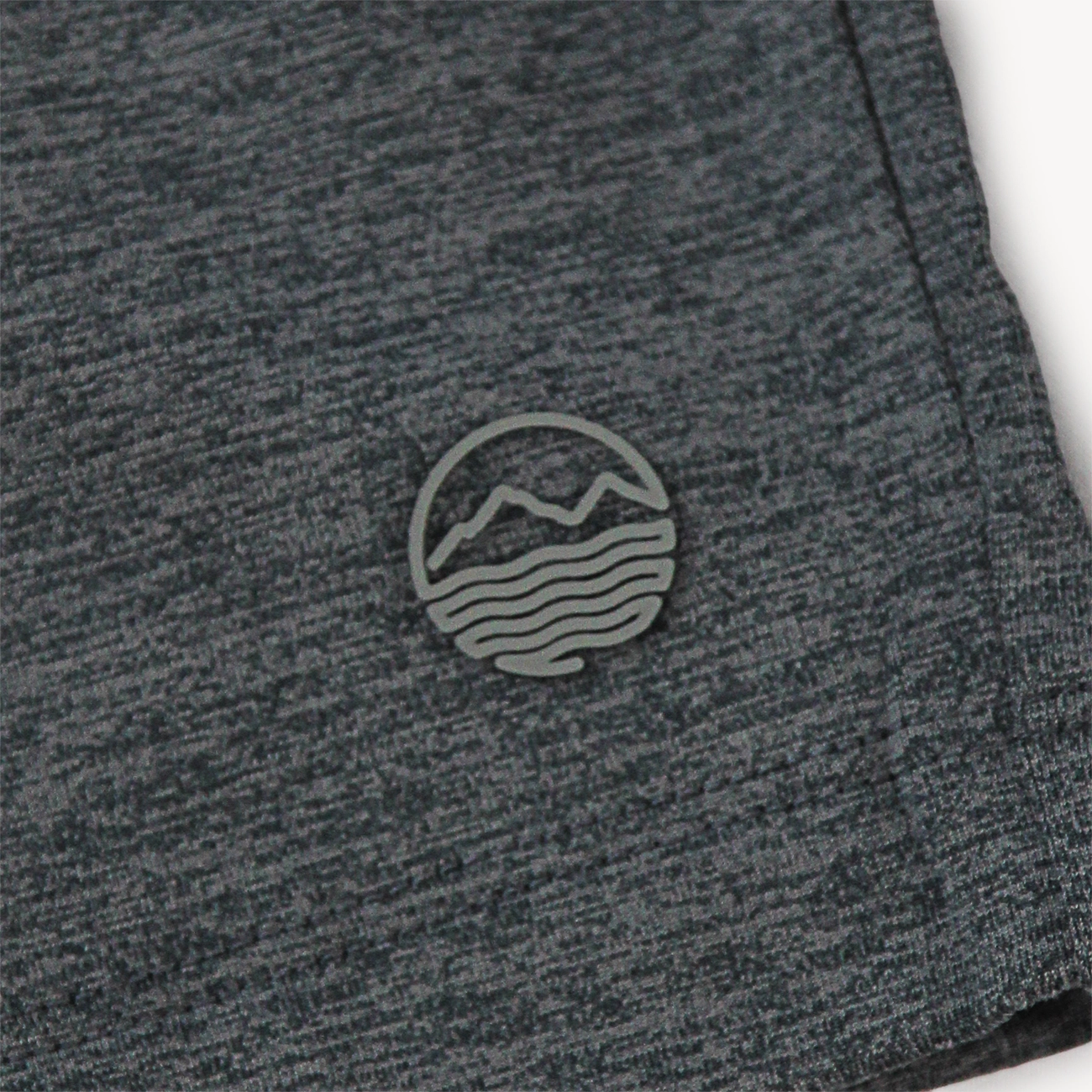 Close-up of a dark heather gray athletic shorts for men with a small circular gray mountain-and-wave logo patch on the side.
