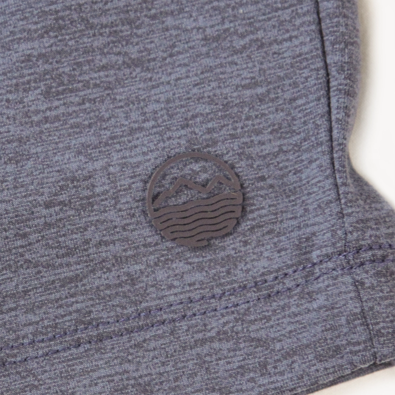 Close-up of a heather gray athletic short for men with a small dark gray circular mountain-and-wave logo patch on the side.