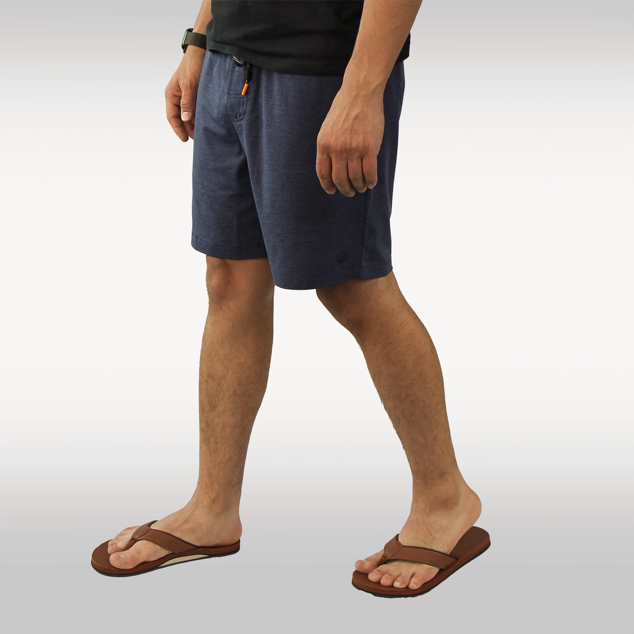 A person wearing dark heather gray drawstring shorts with side pockets, paired with tan Hari Mari flip-flops and a black top, shown from the waist down against a light gray studio background.