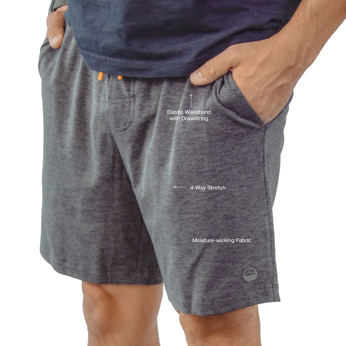 A close-up of a person wearing heather gray athletic shorts with hands in pockets, shown against a white background with text callouts highlighting elastic waistband, 4-way stretch, and moisture-wicking fabric.