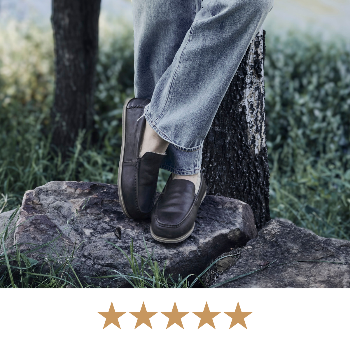 A person wearing light blue jeans and dark brown slip-on loafers stands outdoors on a large rock beside a tree trunk, with a row of five gold stars along the bottom edge.