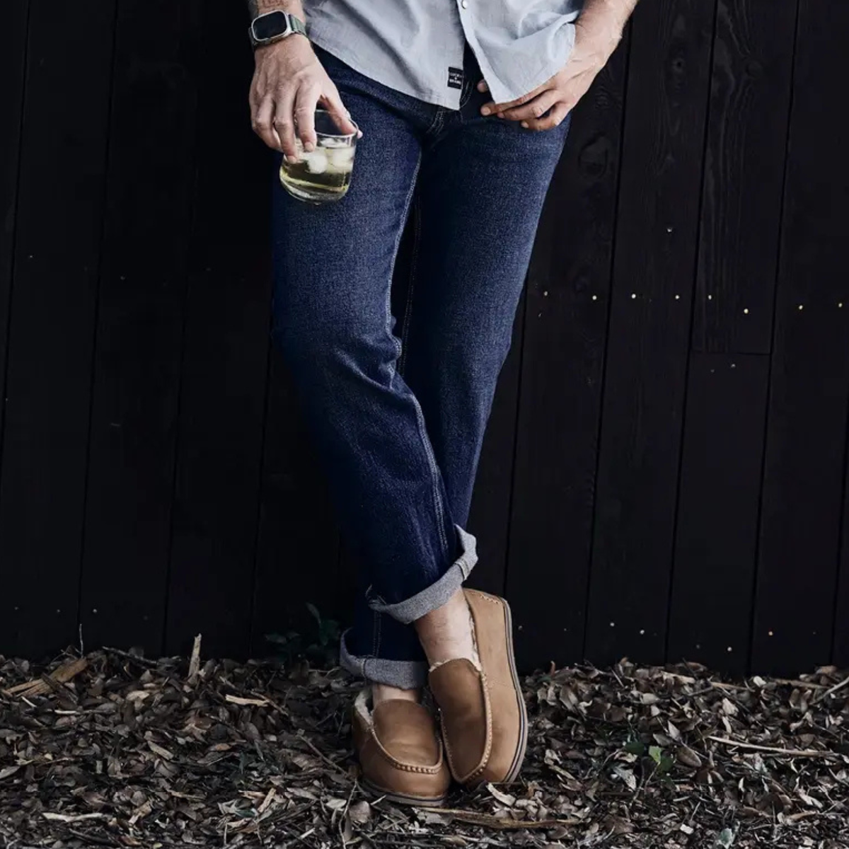 Person wearing tan men's slippers with cuffed jeans outdoors.