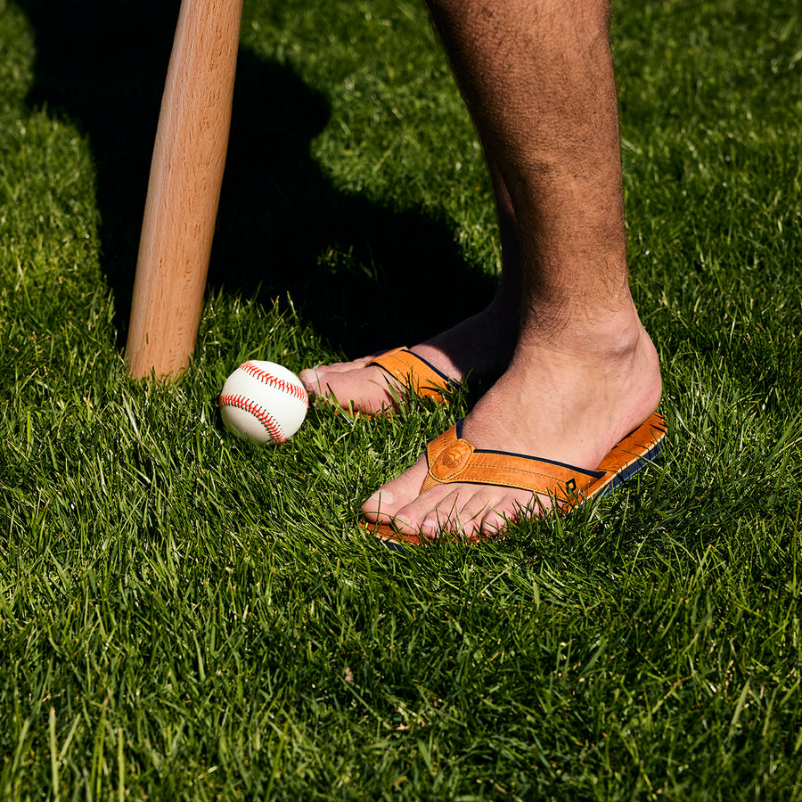 Person wearing Nokona x Hari Mari flips on grass with a baseball and wooden bat