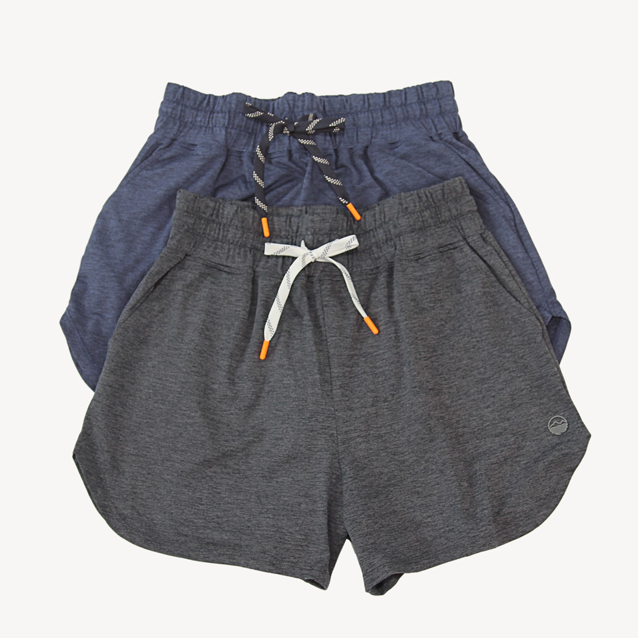 Three pairs of Hari Mari women's athleisure shorts stacked together on a light background. The front pair is heather dark gray with a white drawstring and orange tips, the middle pair is navy blue with a gray and white drawstring, and the back pair is a muted slate blue with a gray and white drawstring.