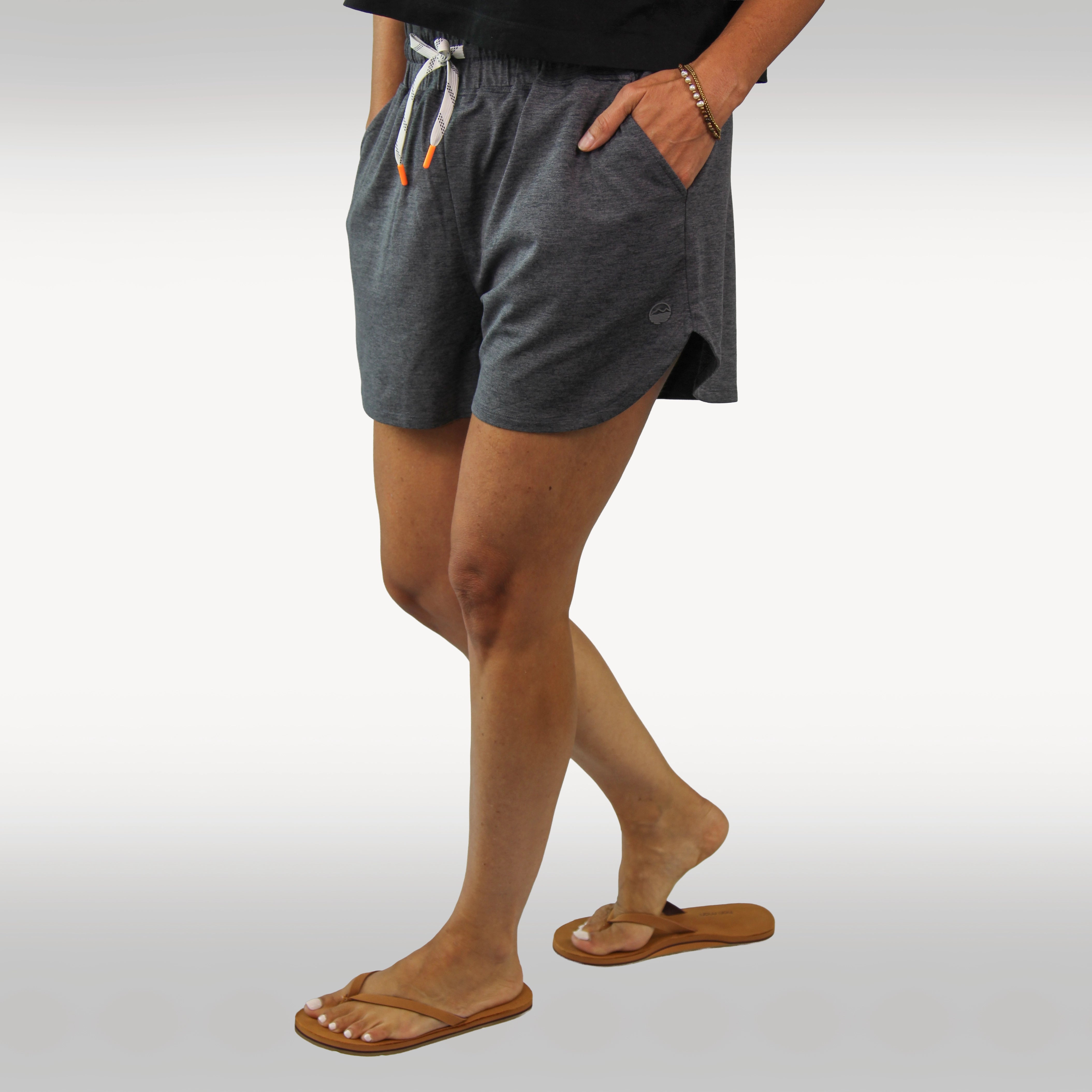 A person wearing dark heather gray drawstring shorts with side pockets, paired with tan Hari Mari flip-flops and a black top, shown from the waist down against a light gray studio background.