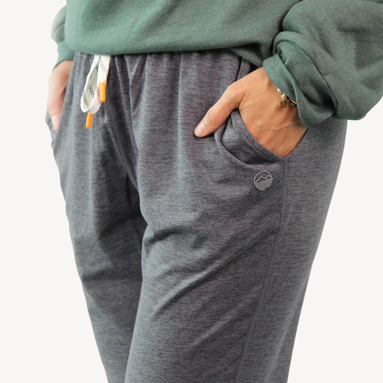 Close-up of a person wearing heather gray joggers from Hari Mari with side pockets, a white drawstring, and a green sweatshirt partially visible.