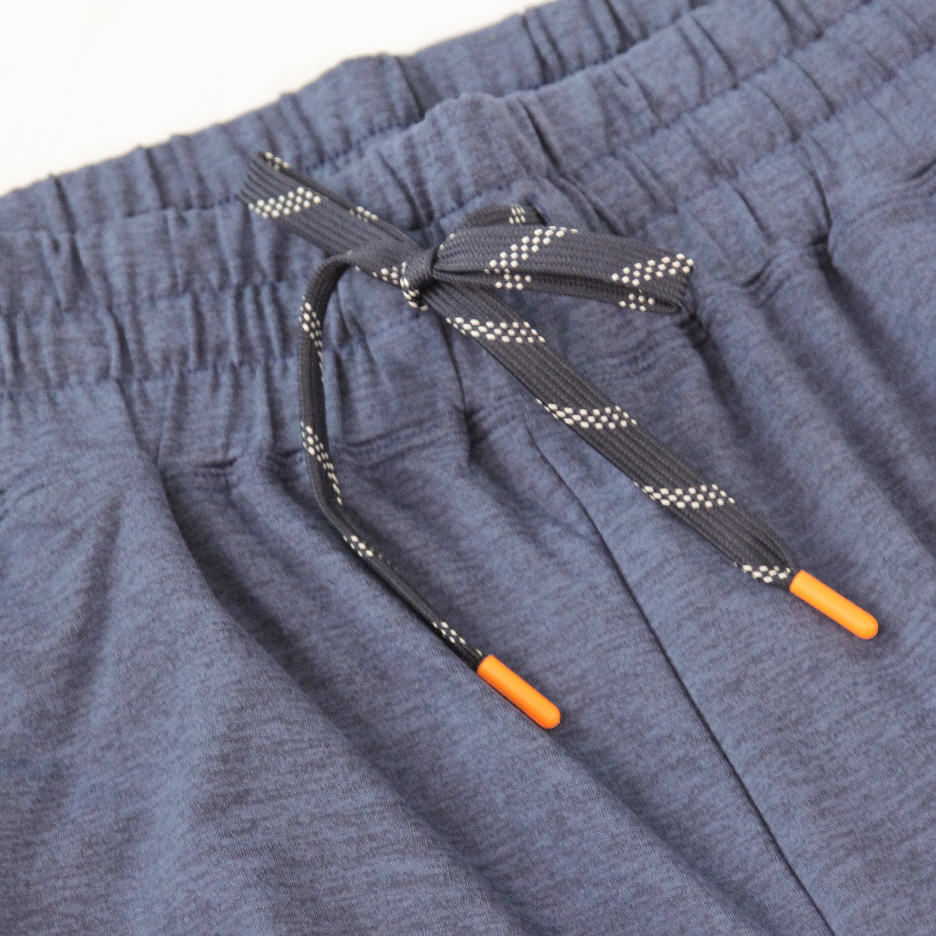 Close-up of a pair of heathered navy drawstring joggers from Hari Mari, showing the elastic waistband, a patterned dark gray drawstring with white dots, and bright orange tip caps.