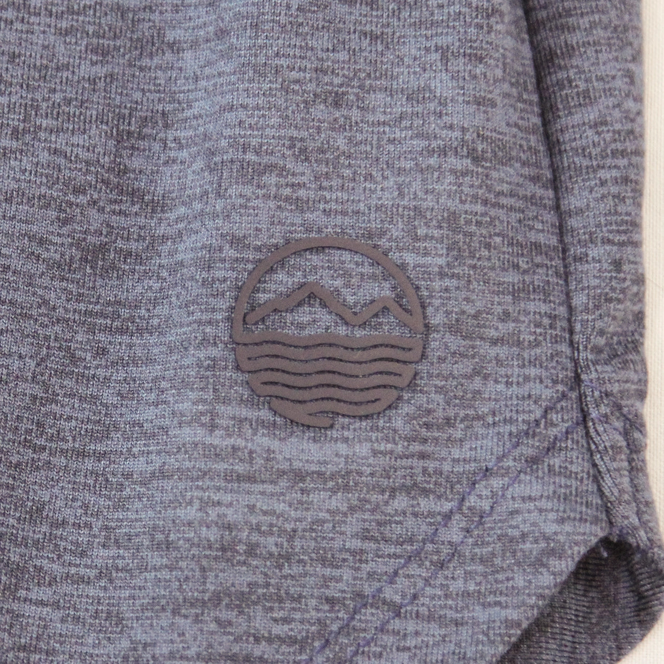 Close-up of heather gray athletic shorts with a Hari Mari logo patch on the side.