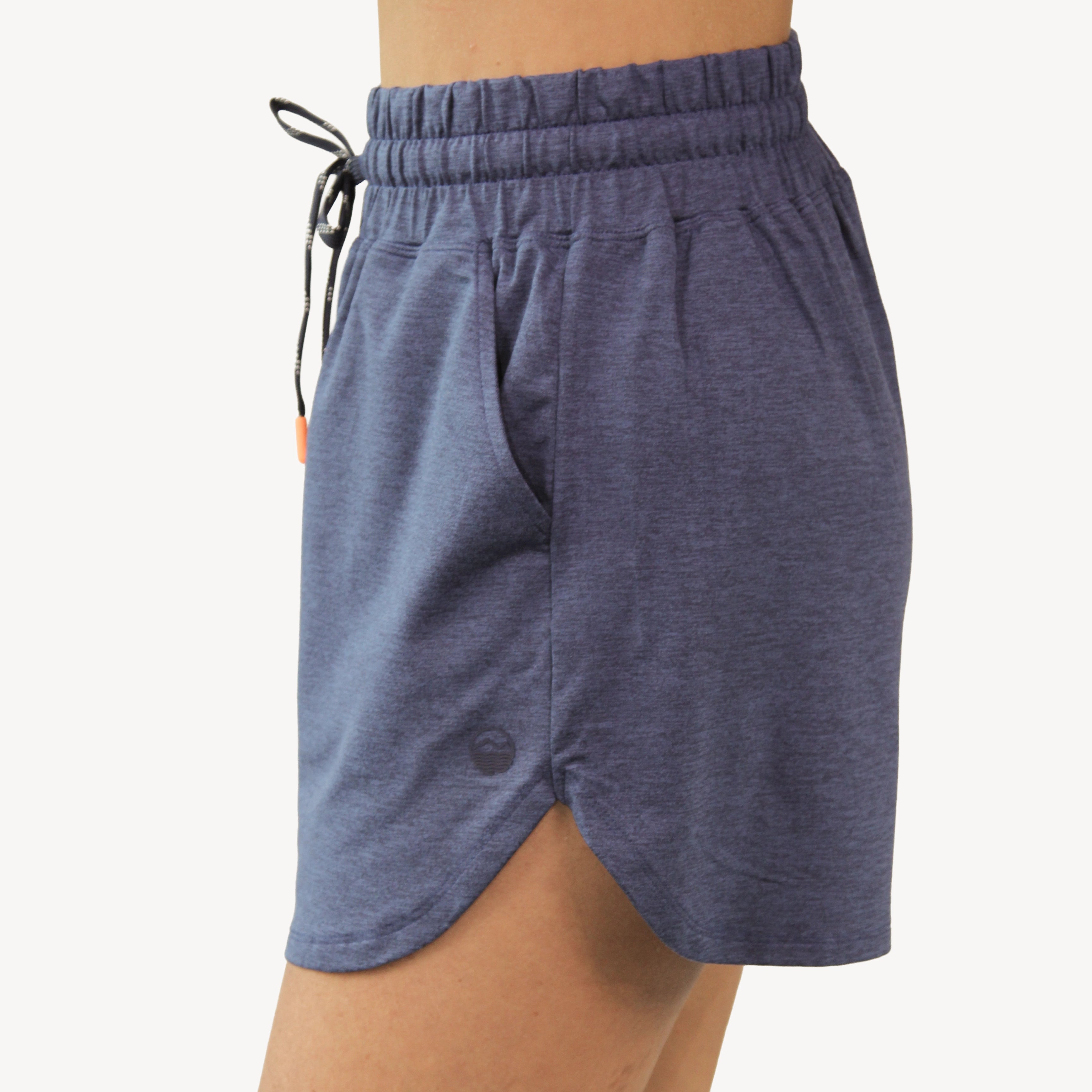A close-up of a woman wearing heathered navy athletic shorts from Hari Mari with an elastic drawstring waistband and a side button detail, against a plain off-white background.