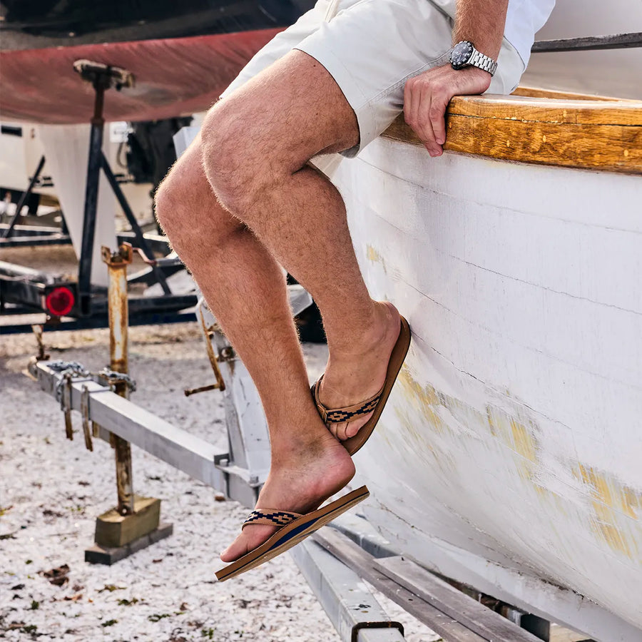 man sitting on side of a boat wearing leather Hari Mari flip flops for men