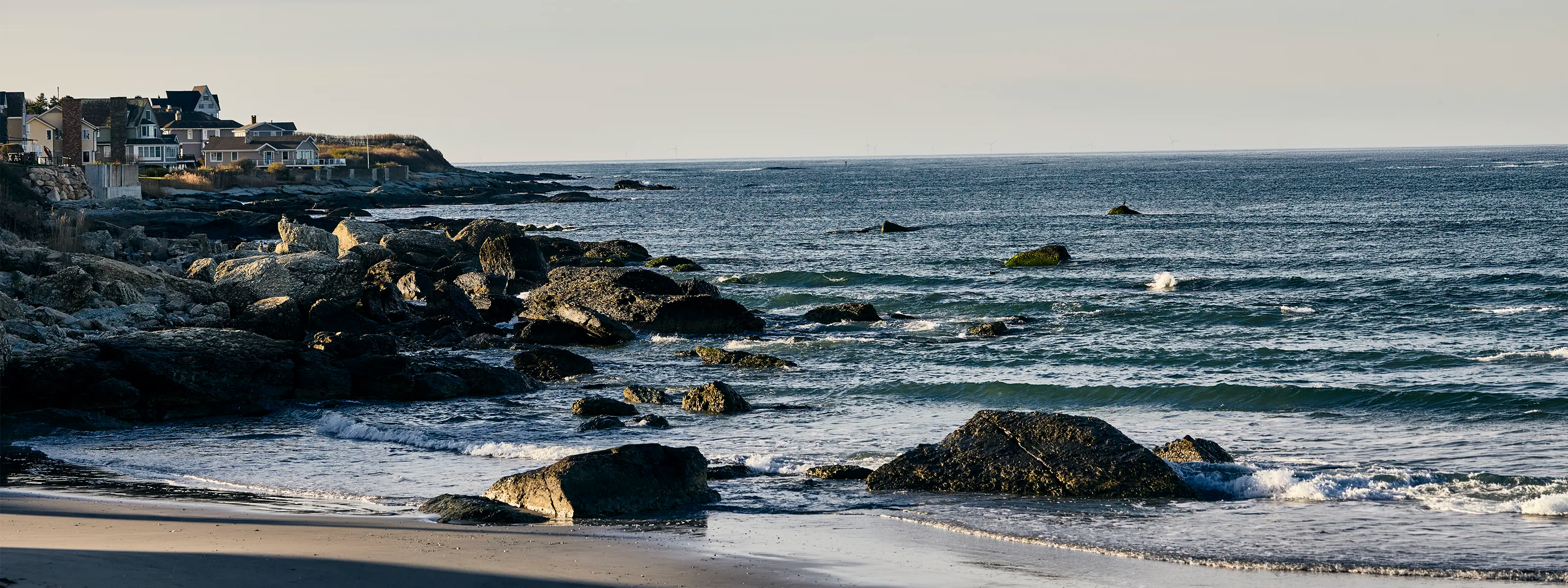 Coastal scene with rocks and ocean waves near a cityscape.