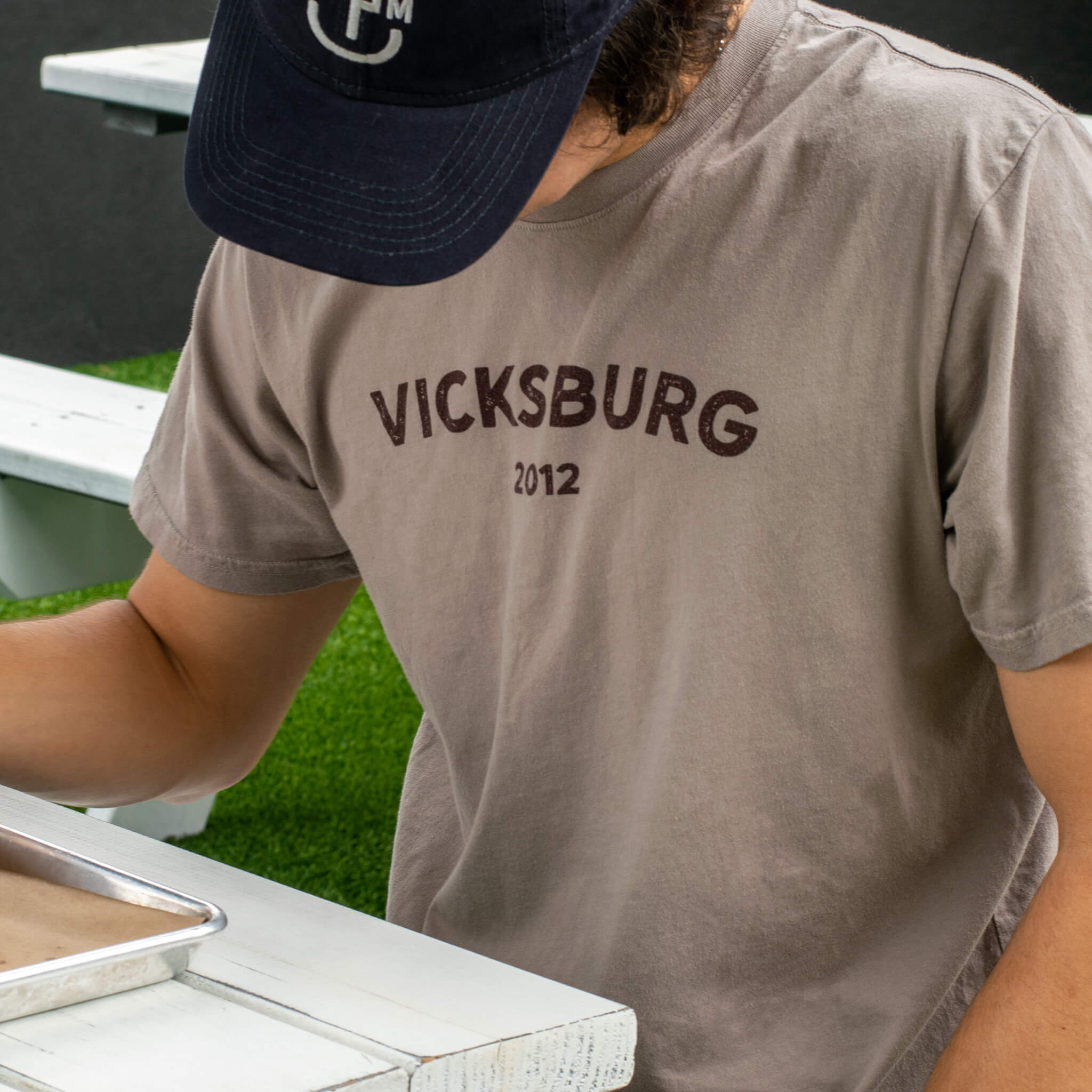 man wearing brown tee shirt with maroon graphic on chest at picnic table at lunch